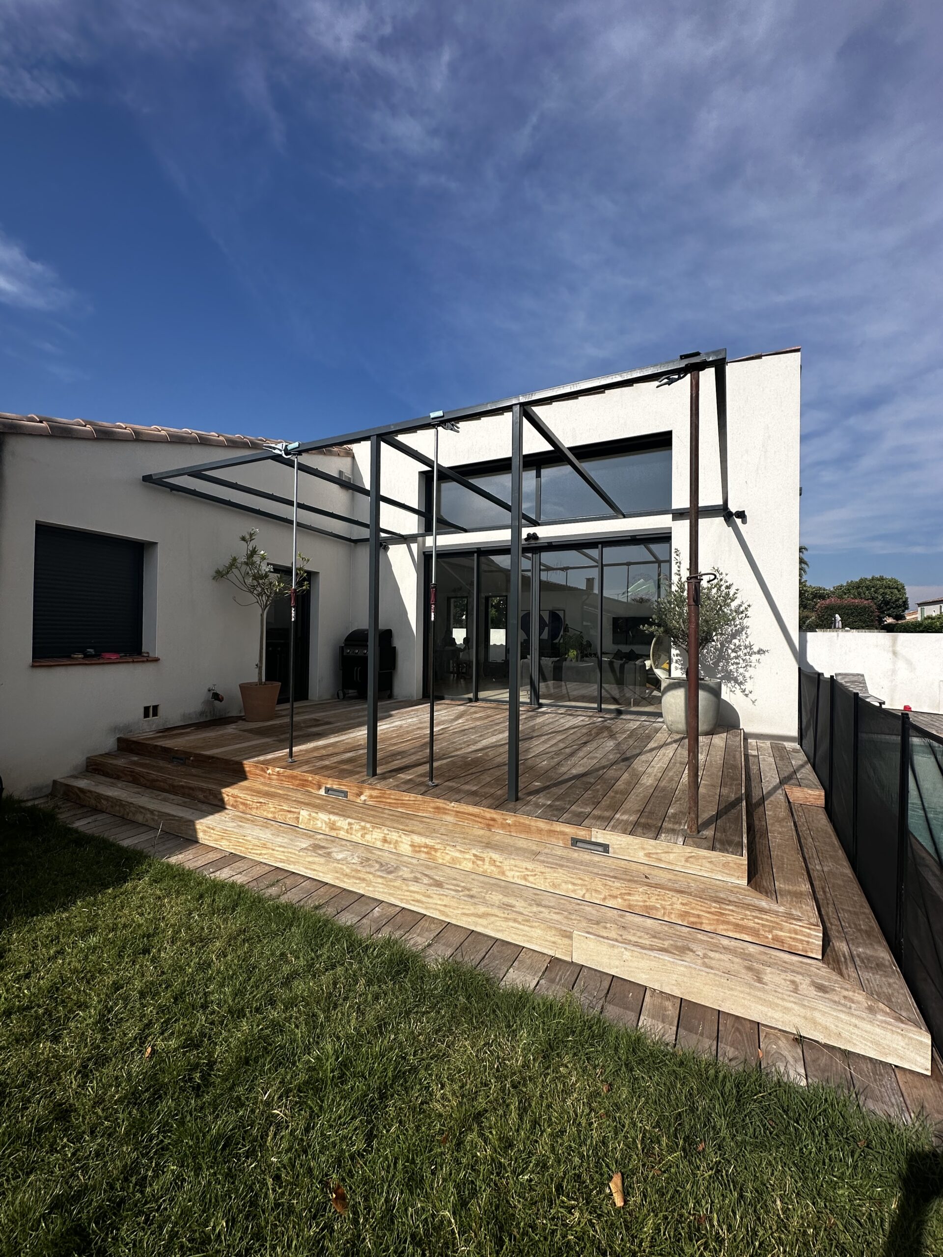 Pergola en acier gris anthracite couverte de canisses au-dessus d'une terrasse bois en bord de piscine à Mauguio, Métallerie Froment