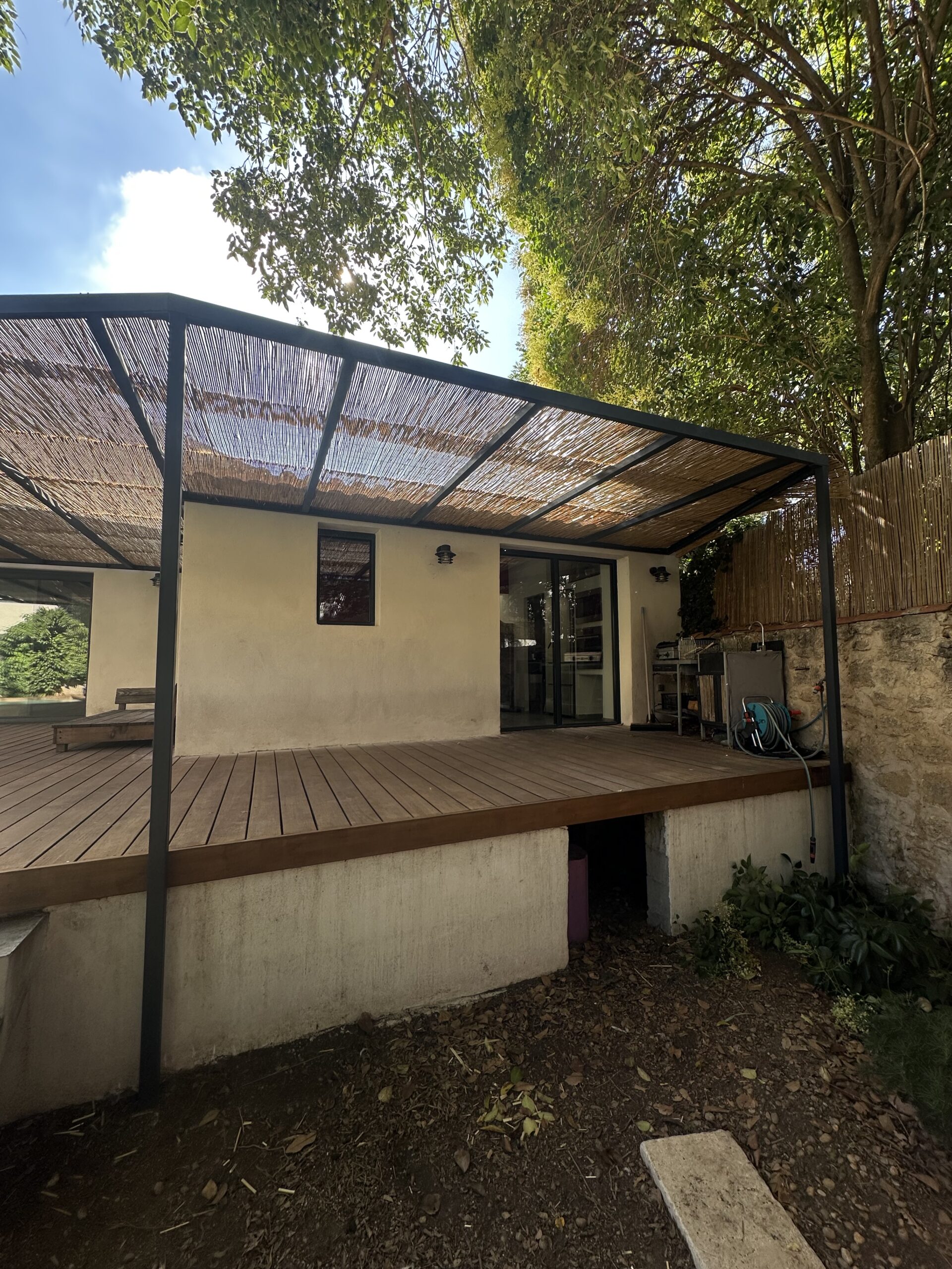 Pergola en acier thermolaqué gris anthracite RAL 7016 couverte de canisses au-dessus d'une terrasse bois à Montpellier